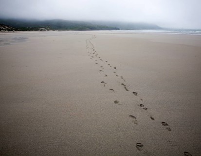 Foot step prints in wet sand on a cloudy overcast day at Traigh Eais beach, Barra, Outer Hebrides,