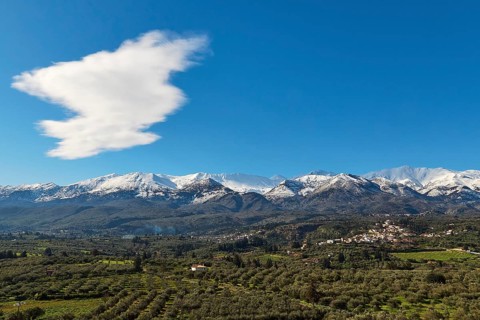 Snow-capped mountains under blue sky and clouds with green valley and village in the foreground,