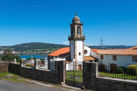 Church with bell tower and closed entrance gate, in the background a hilly landscape and blue sky,