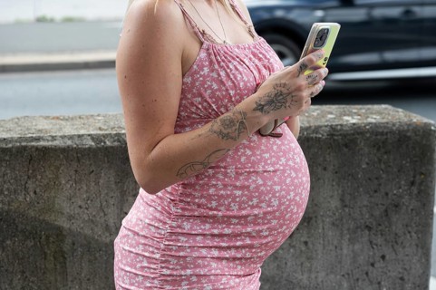Belly of a young pregnant woman with mobile phone, Bavaria, Germany, Europe