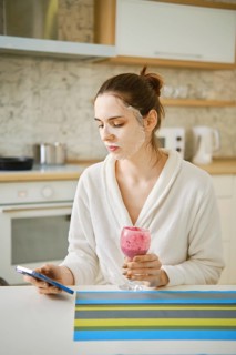 A woman applied a cosmetic mask to her face and spends time sitting in the kitchen with a
