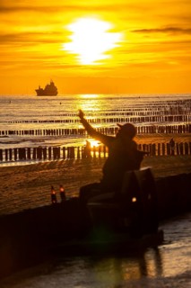 Sunset on the beach of Zoutelande, beach with wooden pile breakwaters, tourists, cargo ship sailing