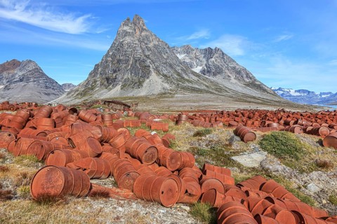 Rusted oil barrels on a fjord in front of steep mountains, remains of a US airbase from the Second