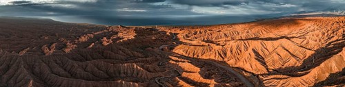 Panorama, landscape of eroded hills, badlands at sunset, Issyk Kul Lake in the background, aerial