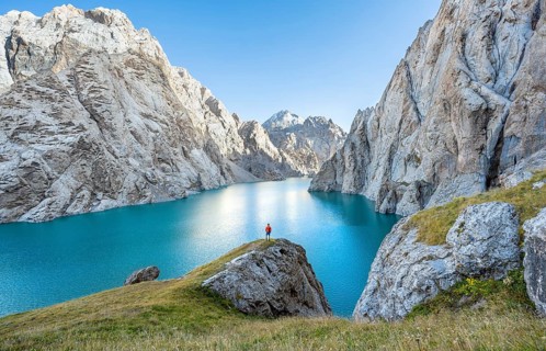 Young man at the turquoise mountain lake Kol Suu with rocky steep mountains, Kol Suu Lake, Sary