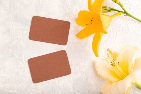 Brown paper business card mockup with orange day-lily flower on gray concrete background. Blank,