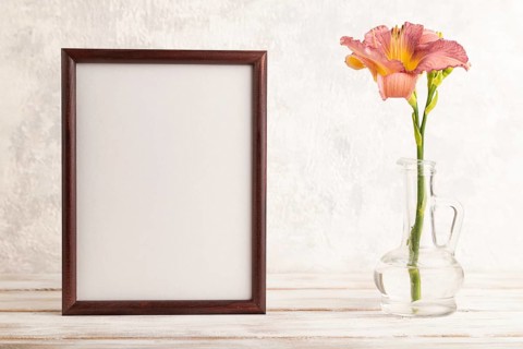 Wooden frame with purple day-lily flowers in glass vase on gray concrete background. side view,