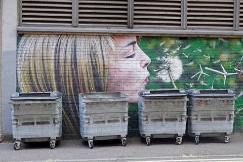 A mural shows a girl blowing a dandelion in front of rubbish containers, Mural Trail, Glasgow,