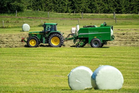Hay harvest, farmer with agricultural machine, picks up mown hay, which is immediately pressed into
