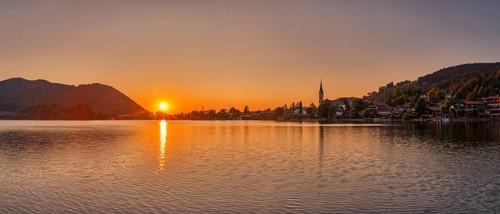 A warm, peaceful sunset picture with a lake, surrounding mountains and a village, Schliersee