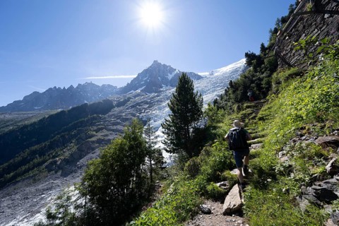 Hiker on hiking trail La Jonction, view of glacier Glacier des Bossons with sun star, behind summit