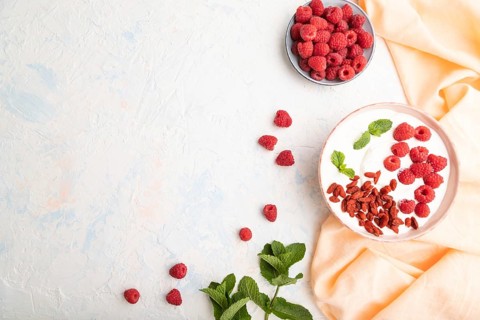 Yogurt with raspberry and goji berries in ceramic bowl on white concrete background and orange