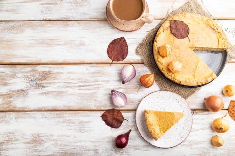 Autumn onion pie decorated with leaves and cup of coffee on white wooden background and linen