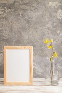 Wooden frame with yellow trout lily or dogtooth violet flowers in glass on gray concrete background