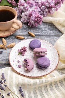 Purple macarons or macaroons cakes with cup of coffee on a gray wooden background and white linen