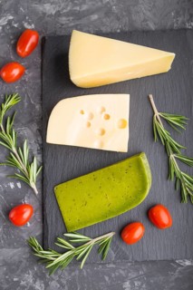 Green basil cheese and various types of cheese with rosemary and tomatoes on black slate board on a