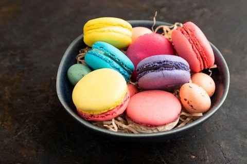 Multicolored macaroons and chocolate eggs in ceramic bowl on black concrete background. side view,