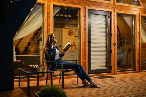 Side view of a woman relaxing on the terrace of modern chalet with a book and an apple in her hands