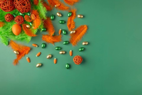 Spring-like Easter arrangement with feathers and chocolate eggs in green and orange on a green
