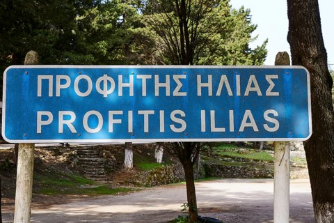 Street sign with Greek and Latin text 'Profitis Ilias' in a natural forest landscape, Profitis