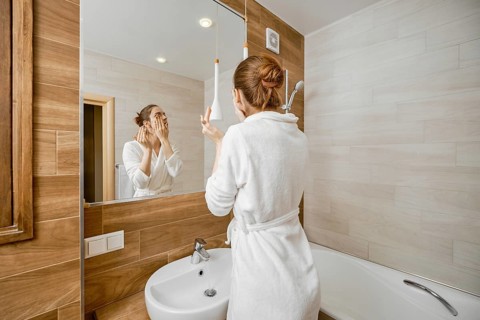 Woman thoroughly washing her face with skin cleanser while standing in a bathrobe in front of a