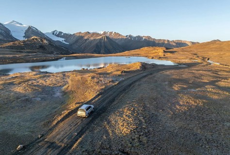 Aerial view, off-road vehicle on gravel track, mountain peak and mountain lake, evening mood,