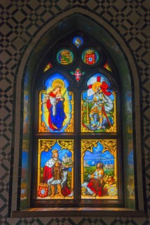 A colourful stained glass window with religious and medieval scenes, depicted in a Gothic stained