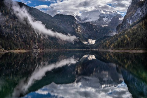 The Vordere Gosausee in autumn. In the background, the Dachstein mountain range in clouds. Partly