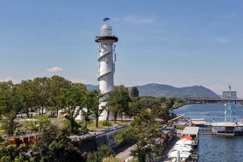 Lighthouse on the riverbank with trees and boats in the background, Vienna