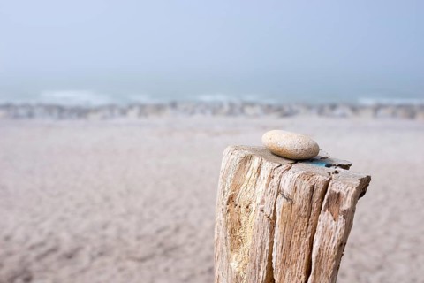 A single stone lies on a wooden pole on the beach with foggy background, pebble on pole, sandy