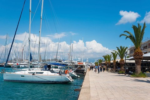 Sailing boats in the harbour next to a promenade under a blue sky with clouds, Mediterranean yacht