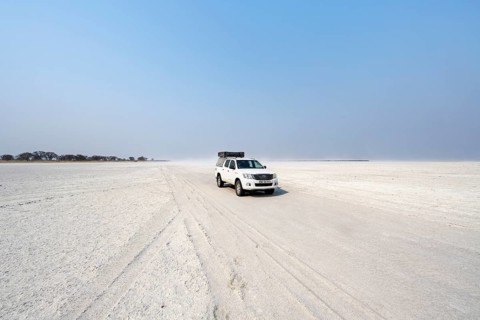 Four-wheel drive Toyota Hilux with roof tent, driving over salt pan, lone car in large wide plain,