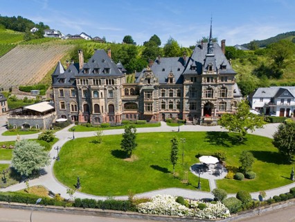 Historic castle with well-tended garden, surrounded by green hills under a blue sky in summer,
