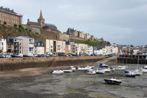 Coastal town with harbour and boats at low water level in front of historic architecture under a