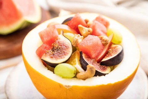 Vegetarian fruit salad of watermelon, grapes, figs, pear, orange, cashew on white wooden background