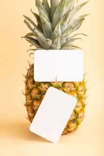White paper business card with ripe pineapple on orange pastel background. Side view, copy space.