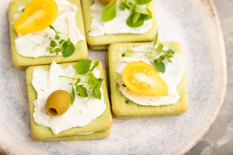 Green cracker sandwiches with cream cheese and cherry tomatoes on gray concrete background. top