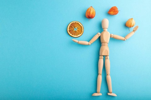 Wooden mannequin juggling dried citrus and physalis on blue pastel background. copy space, isolated