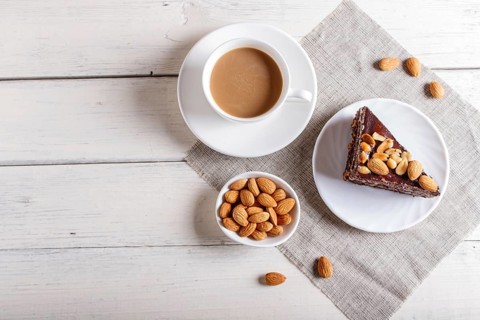 Chocolate cake with caramel, peanuts and almonds on a white wooden background. cup of coffee, top