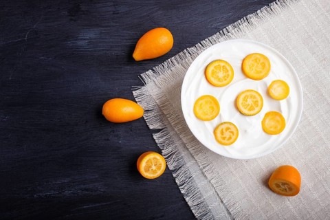 Greek yogurt with kumquat pieces in a white plate on a black wooden background, top view, flat lay,