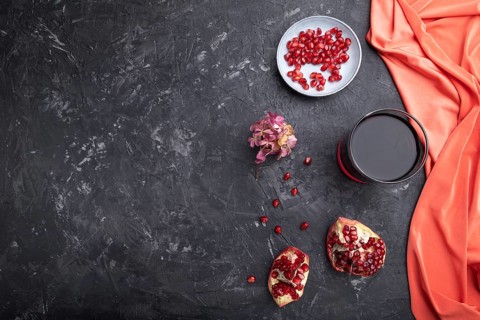 Glass of pomegranate juice on a black concrete background with red textile. Top view, copy space,