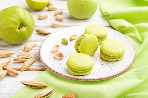 Green macarons or macaroons cakes with cup of coffee on a white wooden background and green linen