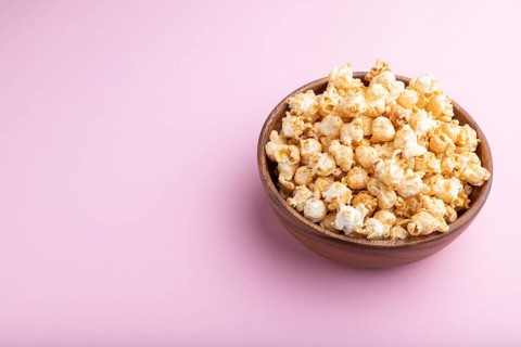 Popcorn with caramel in wooden bowl on a pastel pink background. Side view, copy space