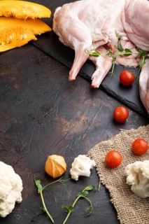 Whole raw rabbit with pumpkin, tomatoes, pea sprouts on a black concrete background and linen