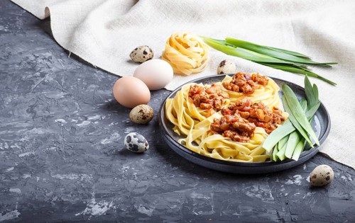 Tagliatelle bolognese pasta with minced meat on a black concrete background. side view, close up,