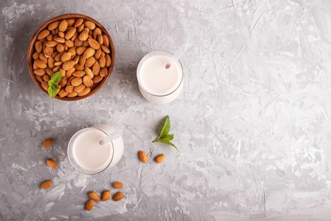 Organic non dairy almond milk in glass and wooden plate with almond nuts on a gray concrete