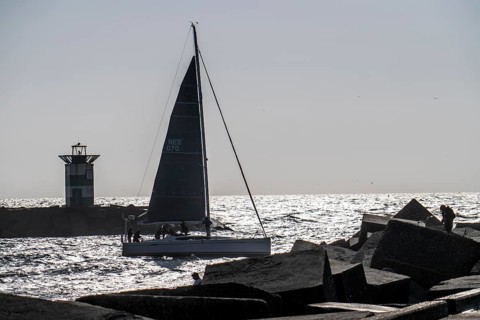 Sailing boat leaving the harbour of Scheveningen, lighthouse at the harbour entrance, Netherlands