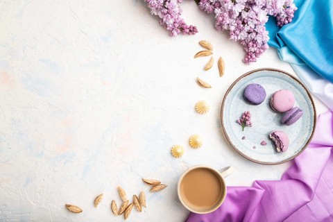Purple macarons or macaroons cakes with cup of coffee on a white concrete background and