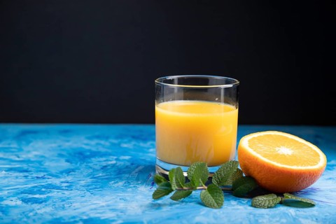 Glass of orange juice with mint on a black and blue background. Hard light, contrast. Side view,