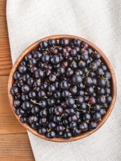 Fresh black currant in wooden bowl on wooden background. top view, flat lay, close up